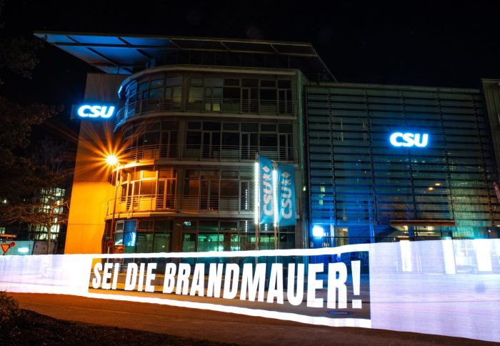 "Sei die Brandmauer" mit Licht gemalt vor der nächtlichen CSU Parteizentrale in München